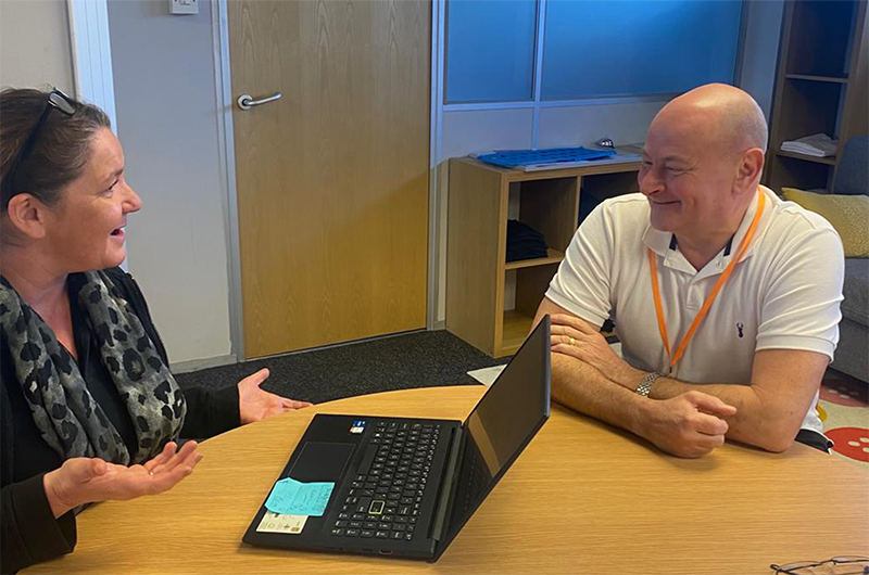 Photograph of a man and a woman at a desk smiling and talking.