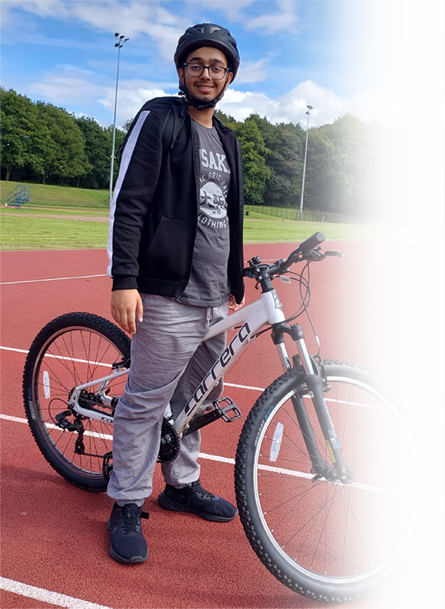 Photograph of a young man outside stood by a bike