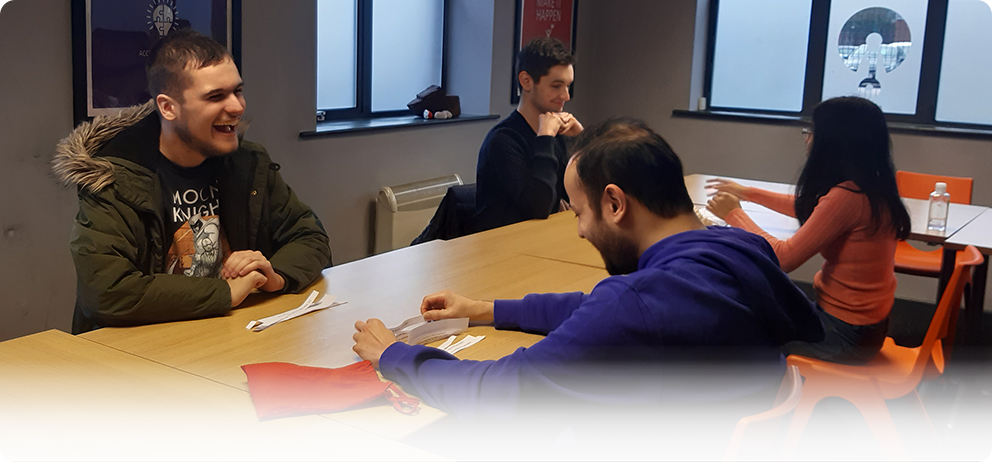 Photo of four people sat at tables, laughing and talking. 